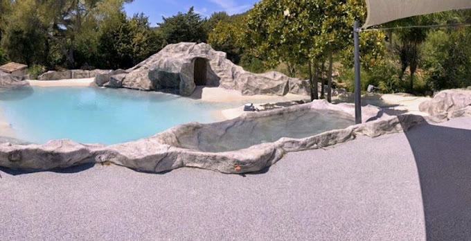 Lagon réalisé avec grotte en rochers sculptés et plage minérale sous voile d'ombrage